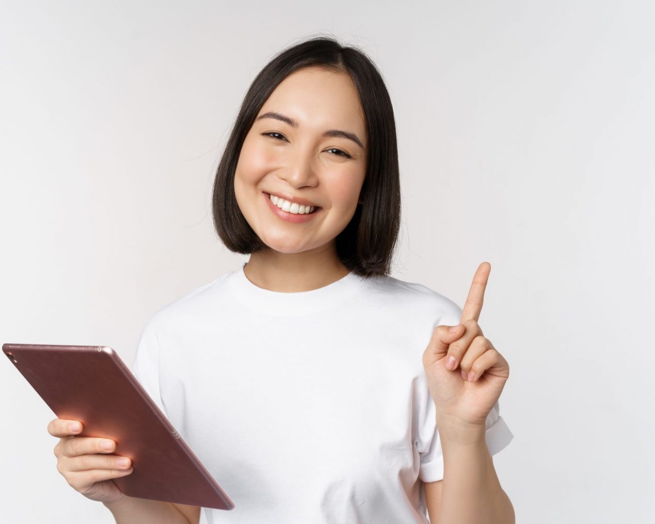 Enthusiastic asian woman with tablet, raising finger and looking amazed, pointing up, standing over white background.